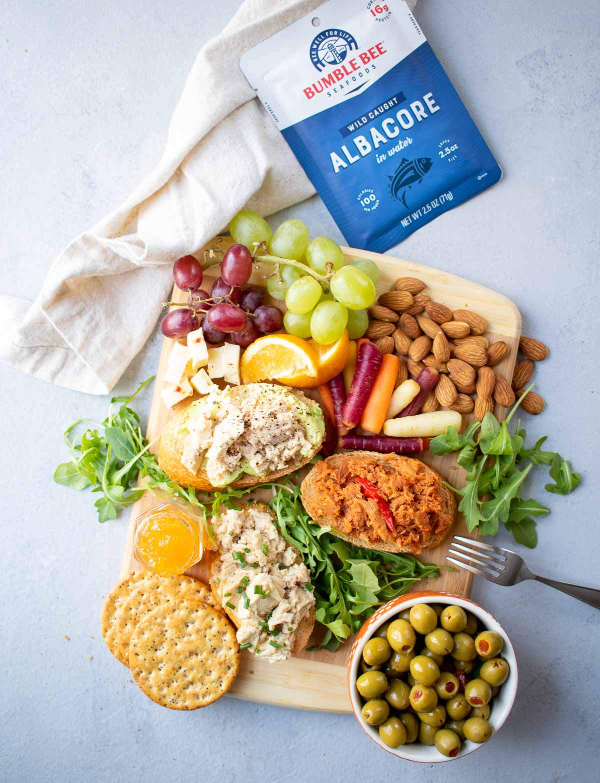 Snack board with tuna toasts, fruit, vegetables, nuts and packets of Bumble Bee Tuna