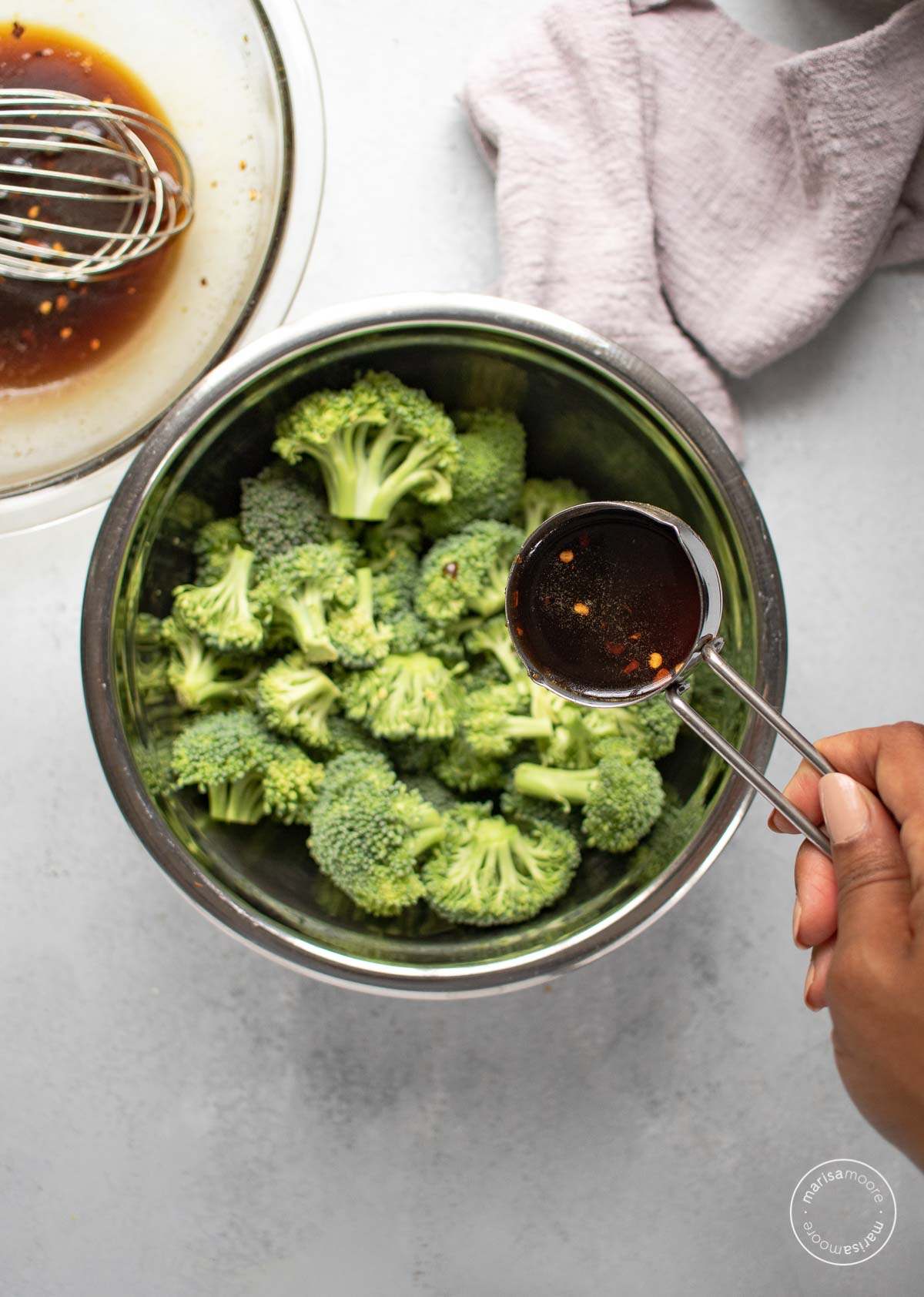 Pouring the sauce onto the broccoli florets in a stainless steel mixing bowl. 