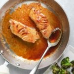 Two filets of black cod in skillet with sauce.