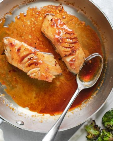 Two filets of black cod in skillet with sauce.