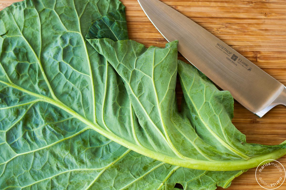 Collard leaves on cutting board with knife.
