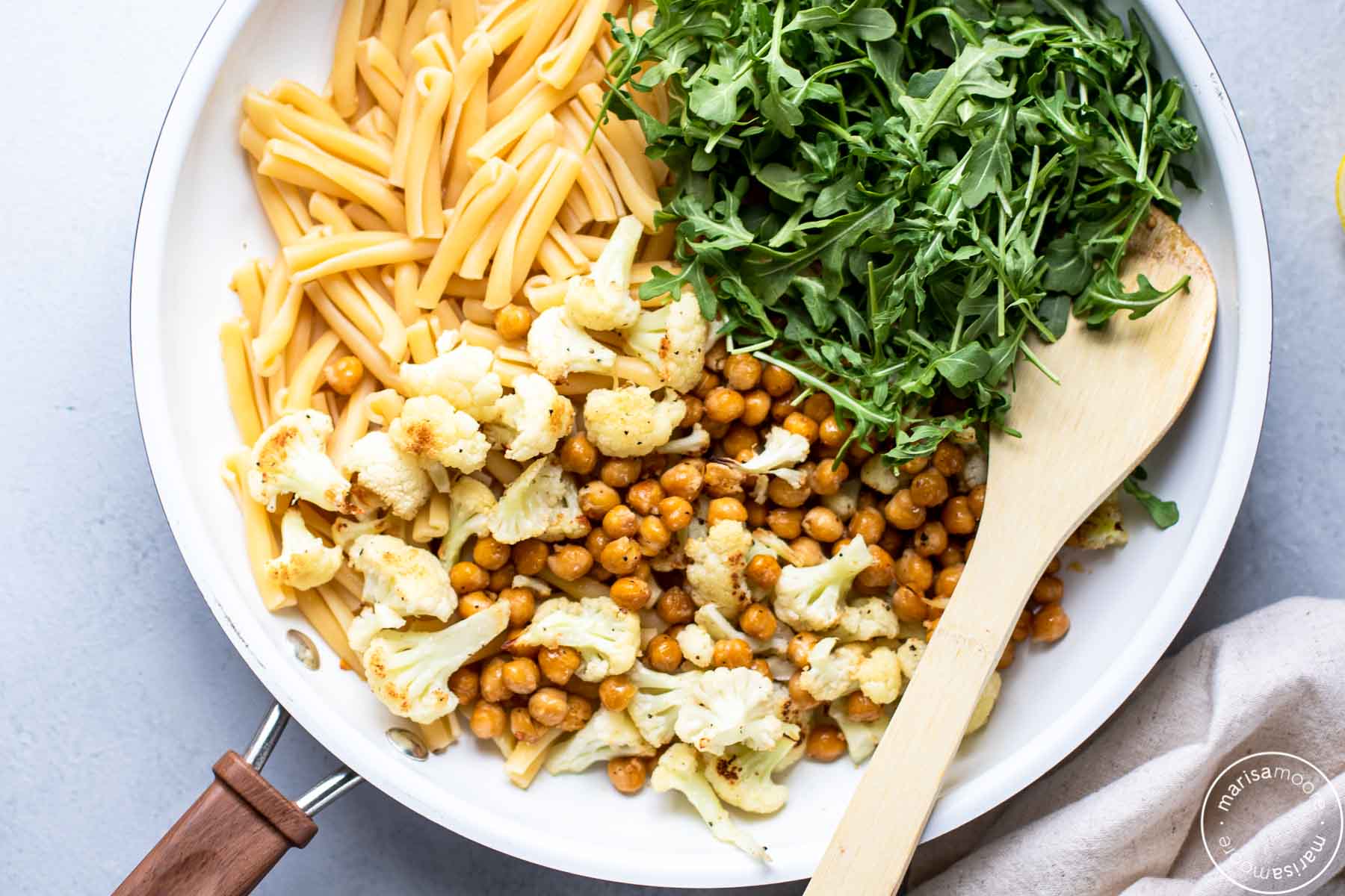 White skillet filled with the pasta and vegetable recipe with a wooden spoon