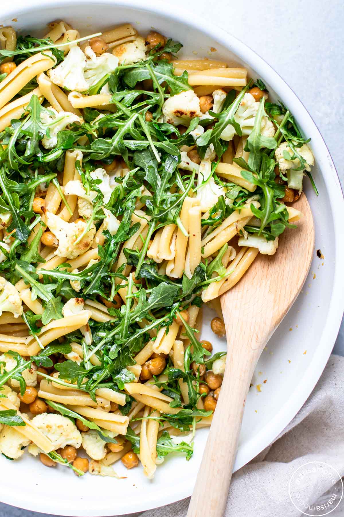 White skillet filled with the pasta and vegetable recipe with a wooden spoon