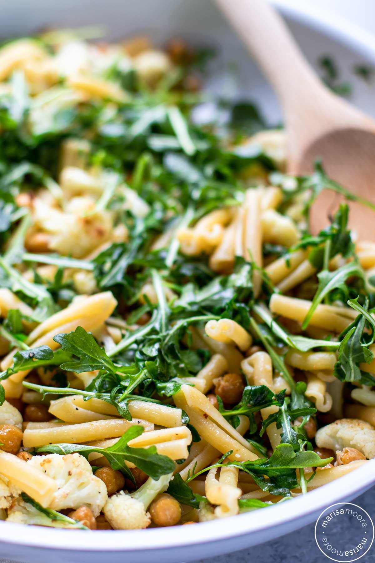 White skillet filled with the pasta and vegetable recipe with a wooden spoon