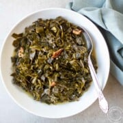 Cooked collards in white bowl with a spoon and a blue napkin