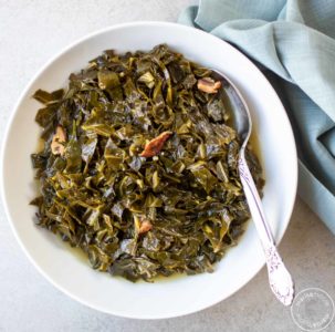 Cooked collards in white bowl with a spoon and a blue napkin