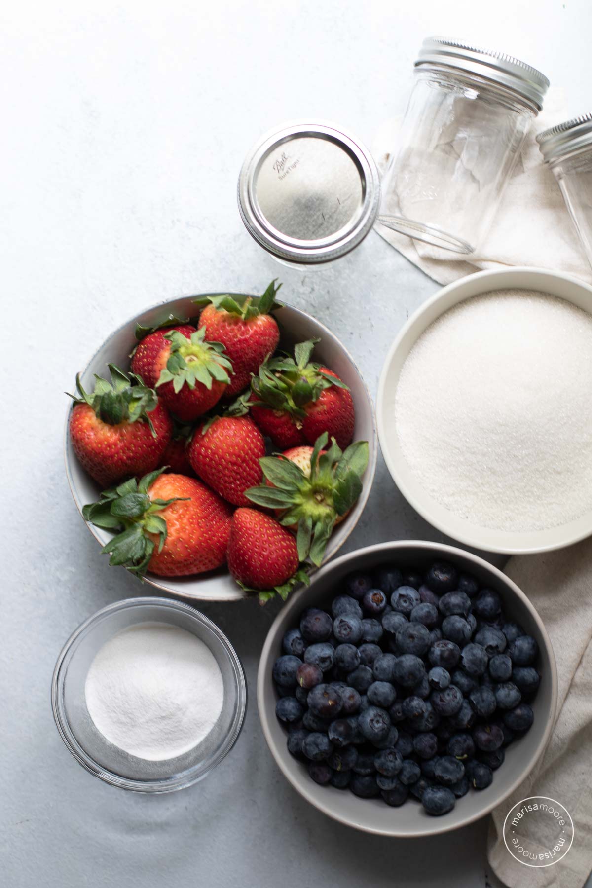 Bowls of strawberries, blueberries, sugar and pectin with 3 empty half pint jars 