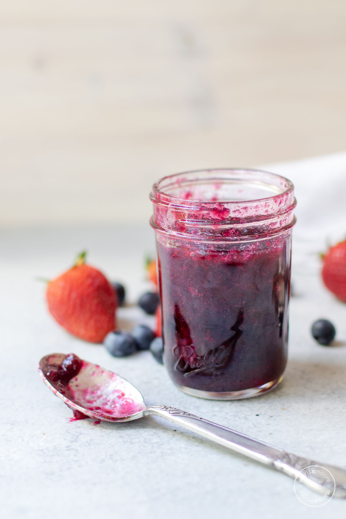 Jam in a jar with berries scattered and a spoon