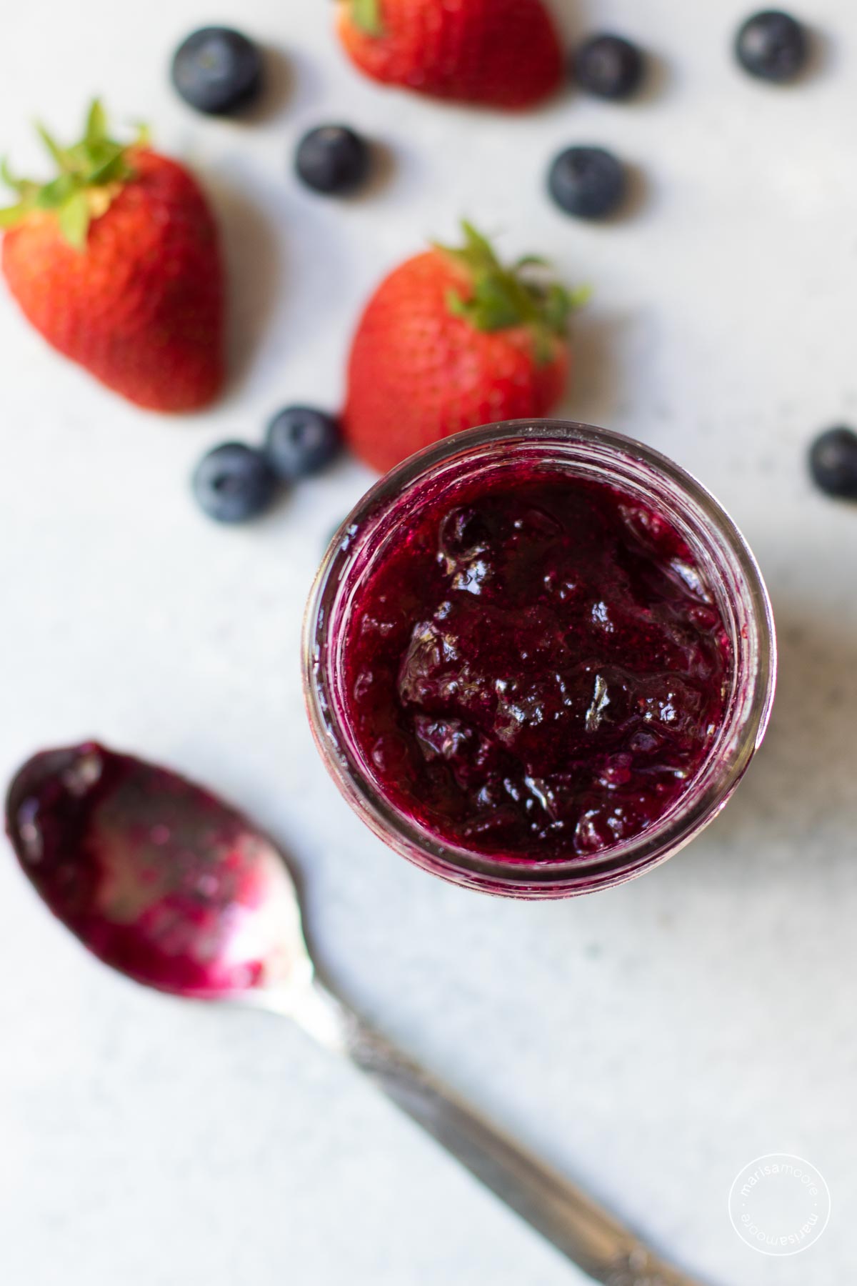 Overhead shot of mixed berry jam in the jar with a spoon alongside it