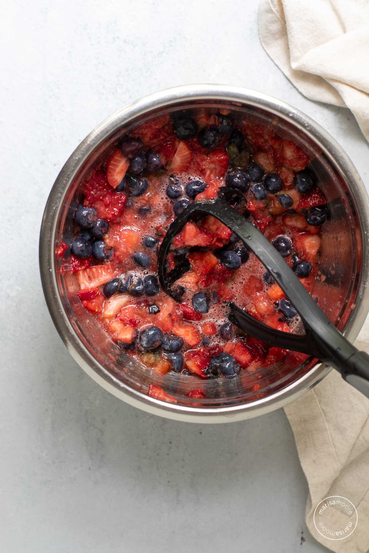 Crushed strawberries and blueberries  in a bowl with a potato masher inside