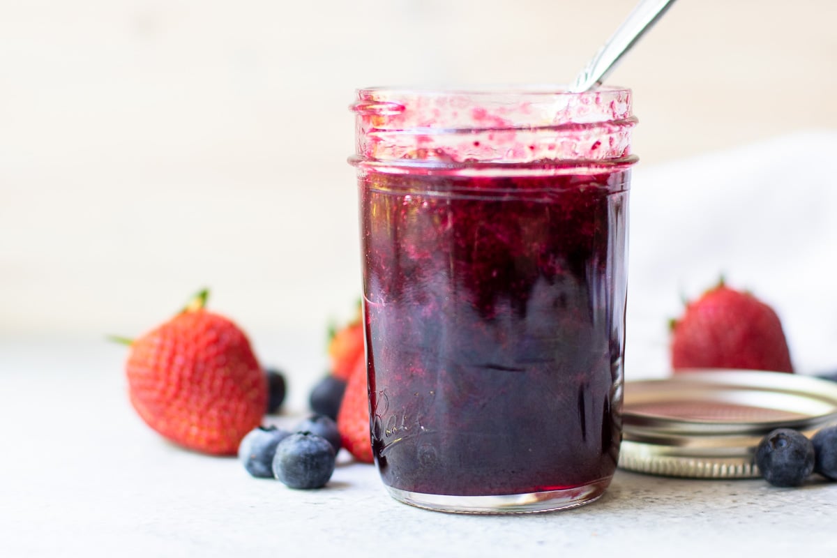 Mixed berry jam in an open jar with a spoon inside 