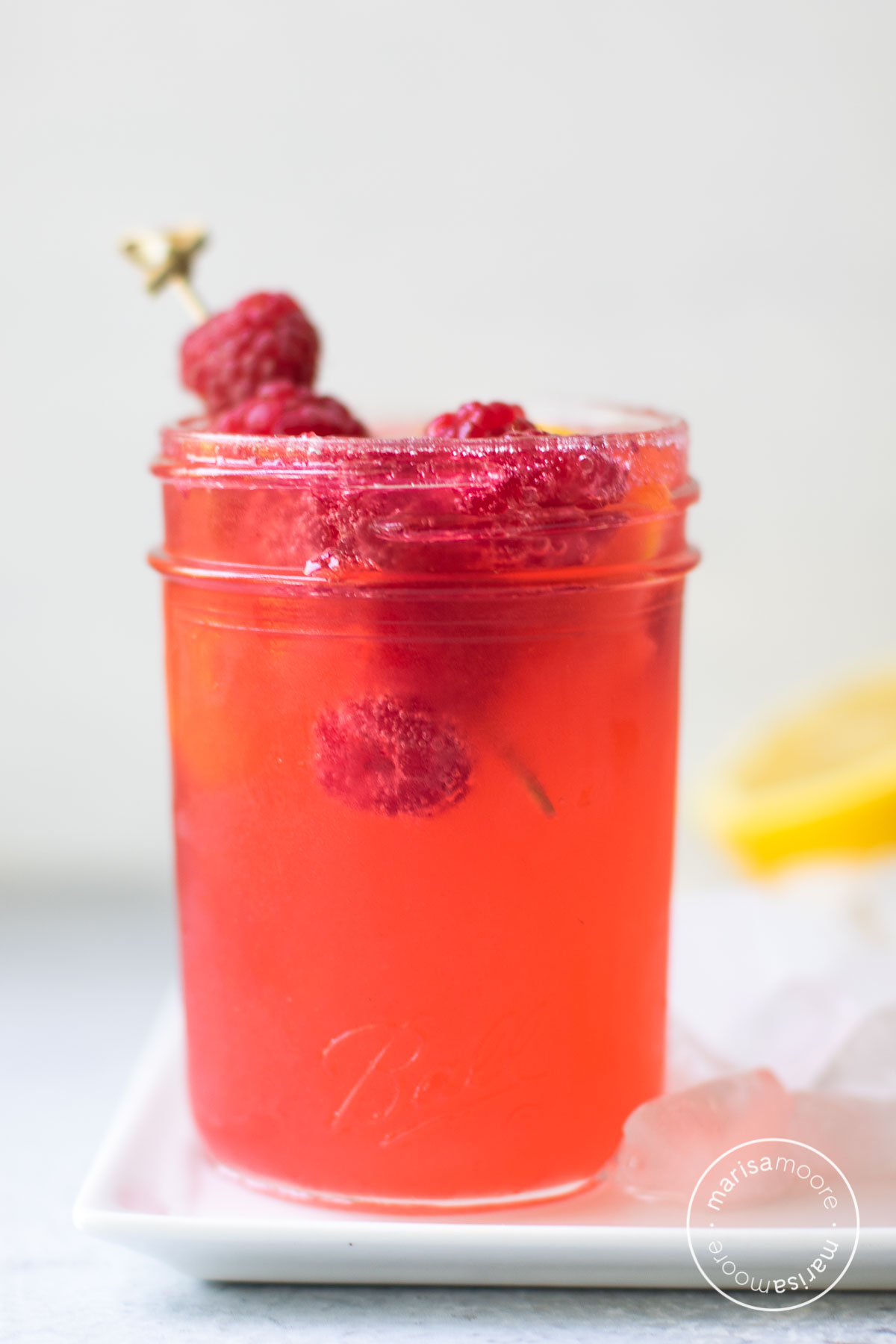 Close up of an 8 ounce jar containing the cocktail with fresh raspberry garnish