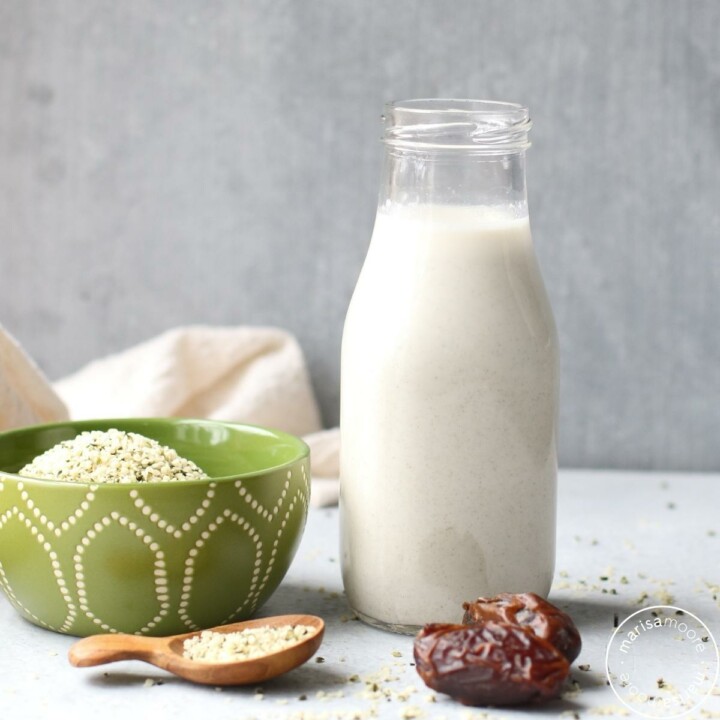 Open bottle of hemp milk, pitted dates, with a green bowl and wooden spoon filled with hemp hearts
