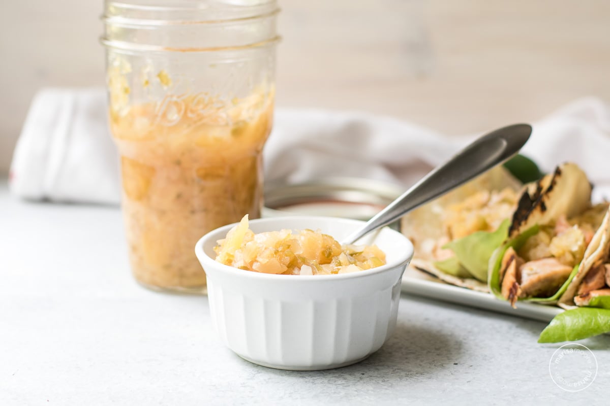 Pineapple relish in a ramekin with tacos in the background