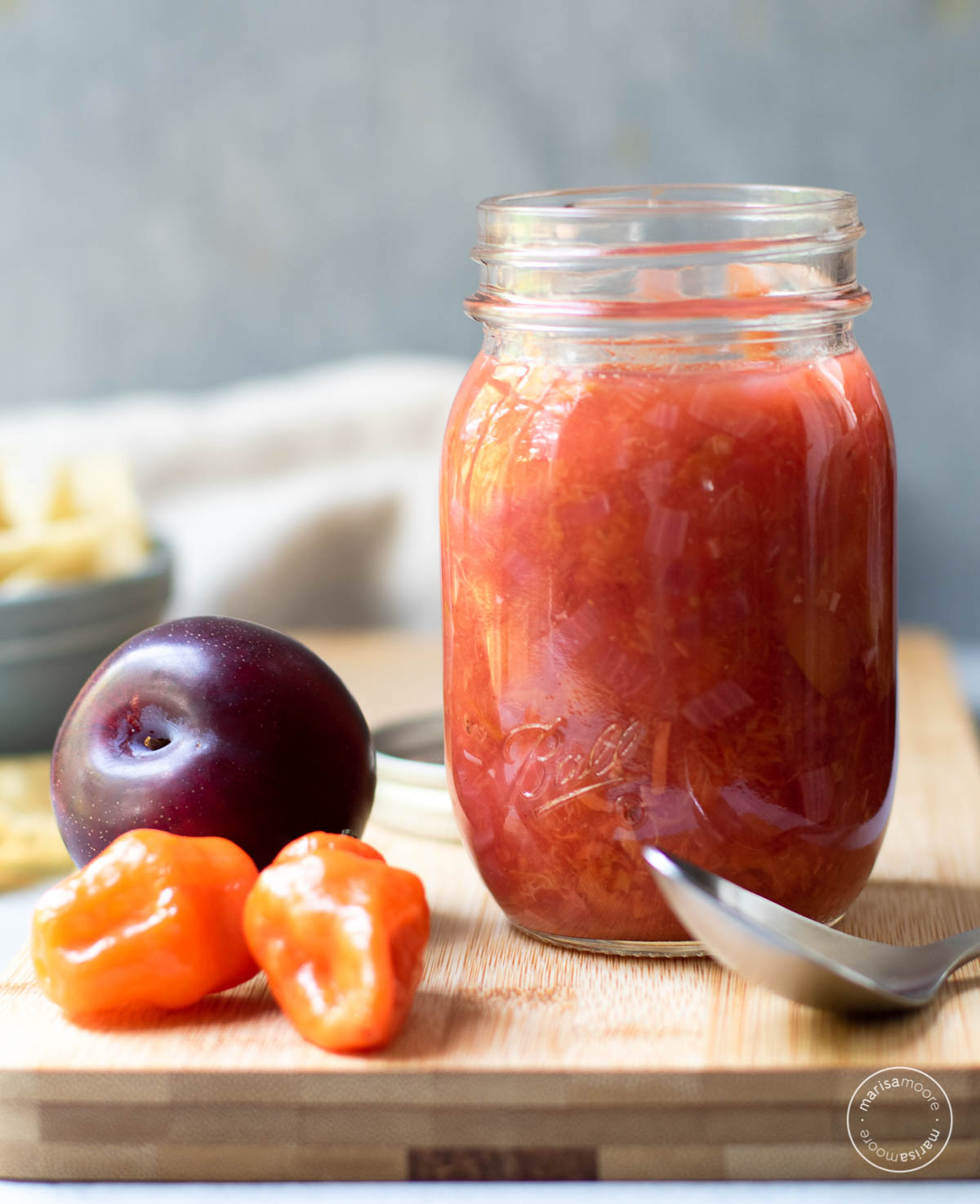 Open jar of salsa with a spoon with peppers and plums next to it