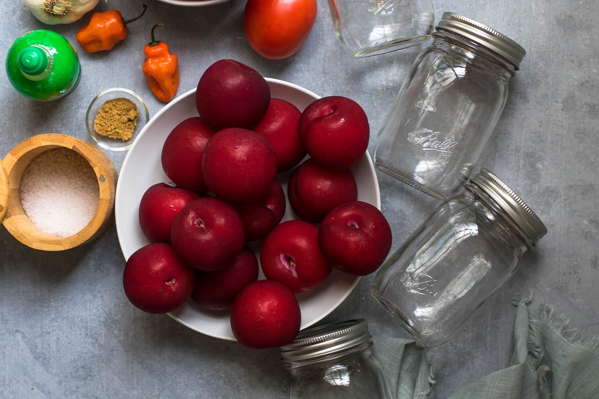 Ball jars with a bowl of plums, salt, habaneros, bottled lime juice and ground coriander