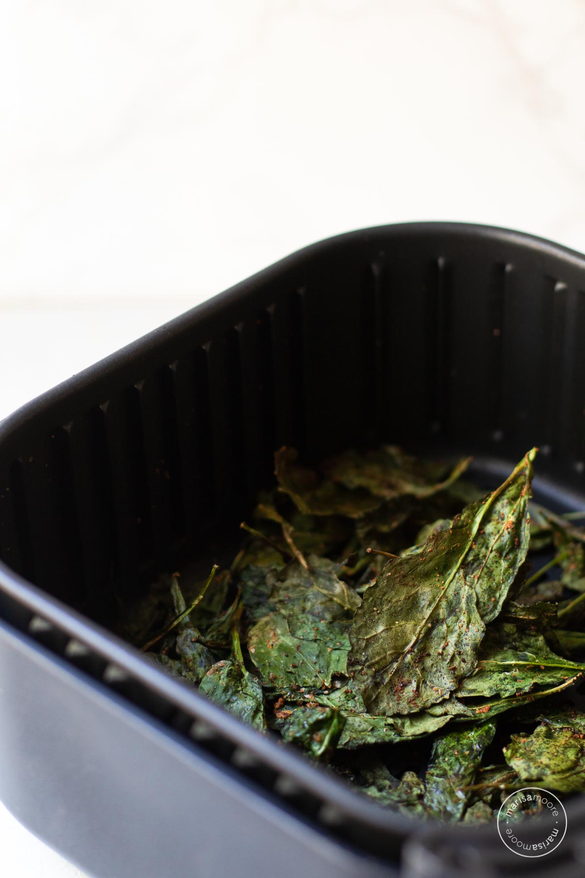 Cooked kale chips in an air fryer basket