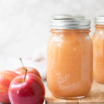 Applesauce in 3 pint jars on a cutting board with red apples