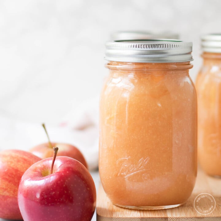 Applesauce in 3 pint jars on a cutting board with red apples