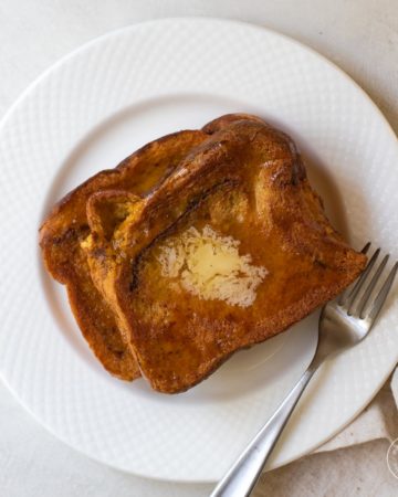 Two pieces of French toast on a white plate with a fork