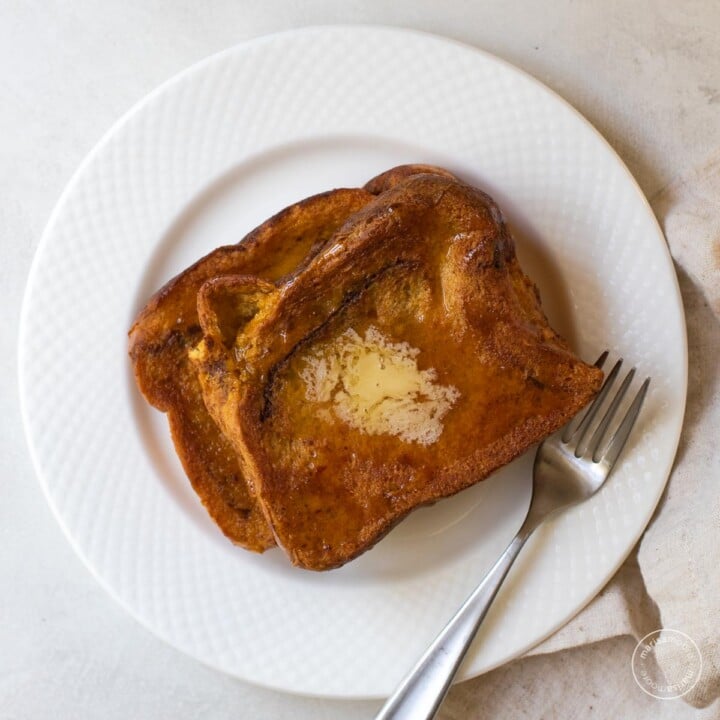 Two pieces of French toast on a white plate with a fork