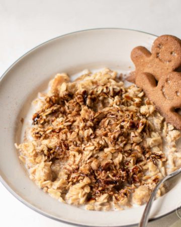 Gingerbread-flavored oats in a bowl drizzled with molasses and garnished with gingerbread people cookies.