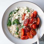 Oats with tomatoes spinach and feta in a grey bowl with a large spoon