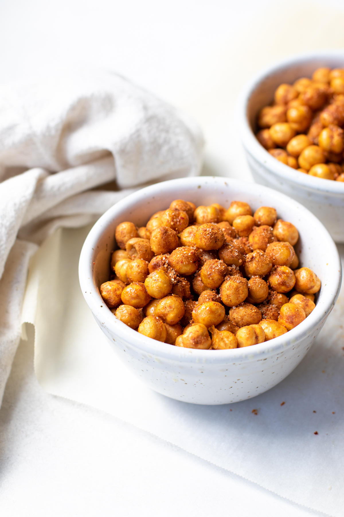 Side view of air fryer chickpeas in a white bowl with beige napkin.