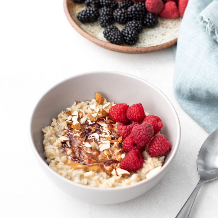 Gray bowl of oatmeal topped with nut butter, jam and raspberries