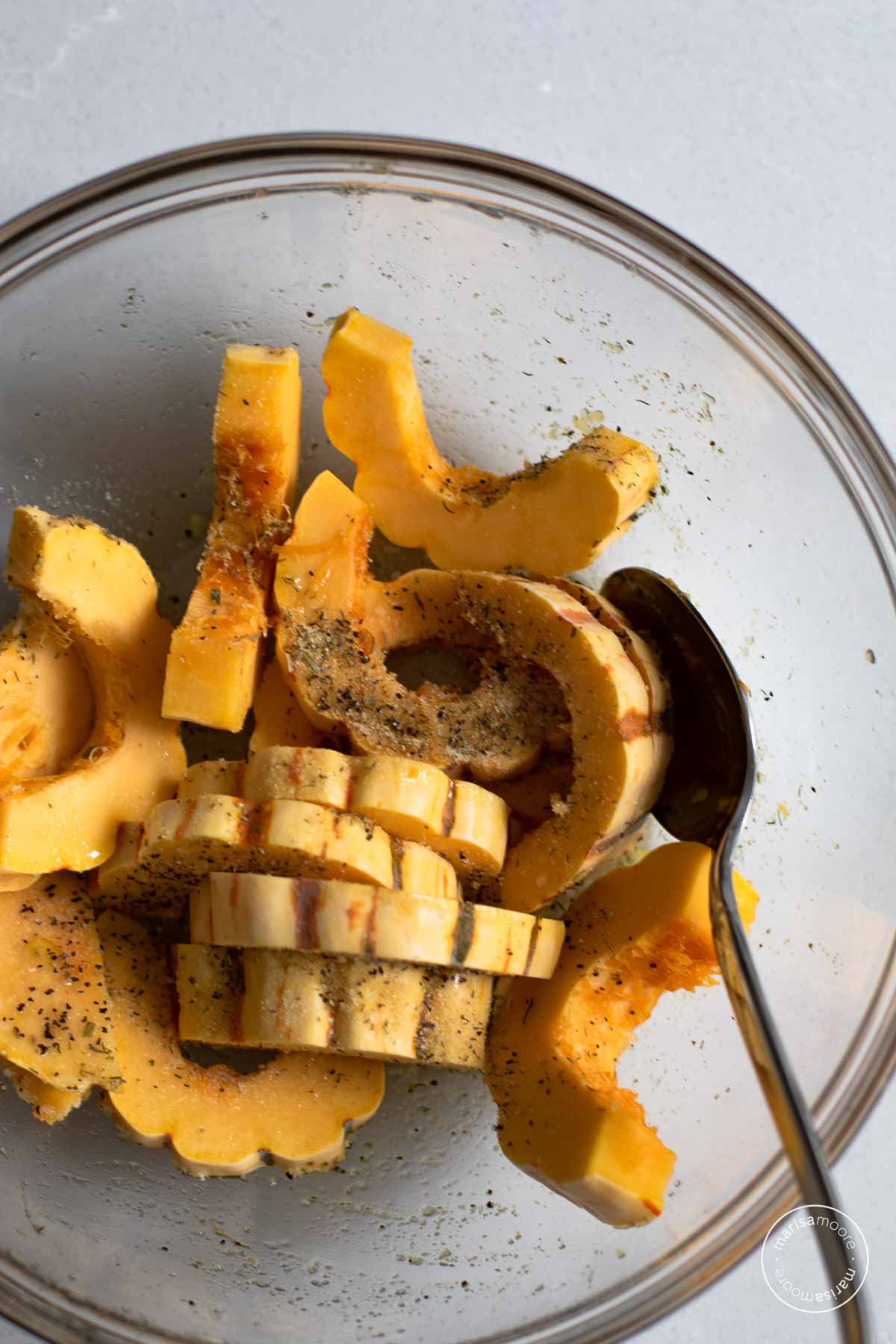 sliced squash in a bowl with the spices and parmesan