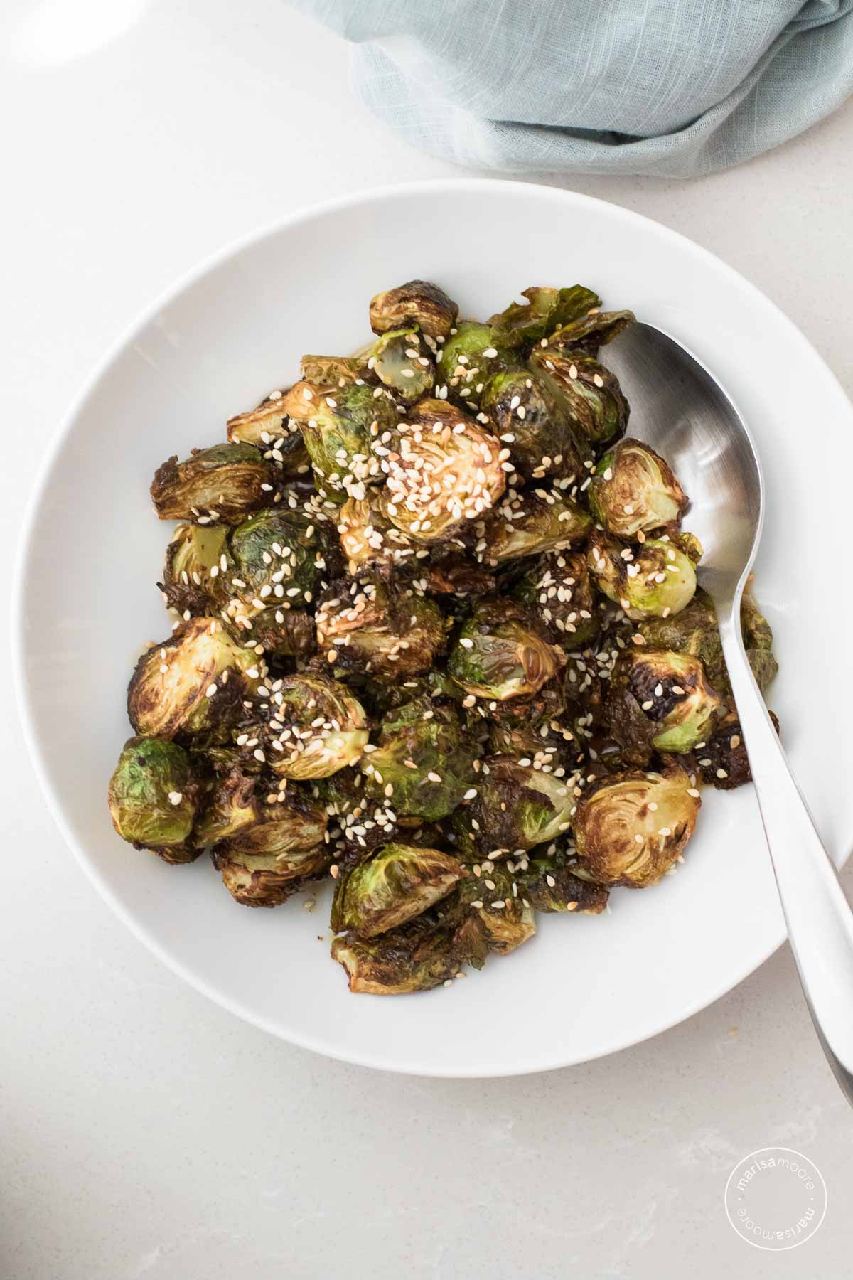 Brussels Sprouts with Sesame Sprinkled in a white bowl with a serving spoon.