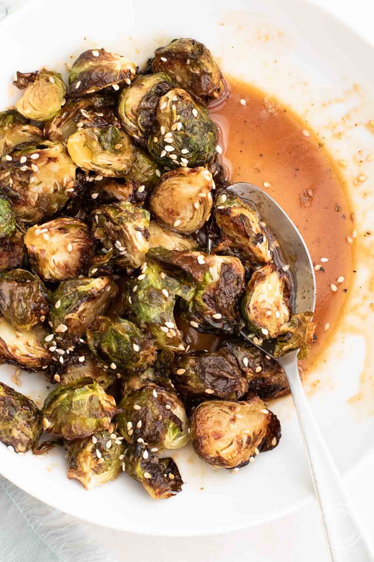 Close up of sauced Brussels Sprouts in a White Bowl with a spoon for serving