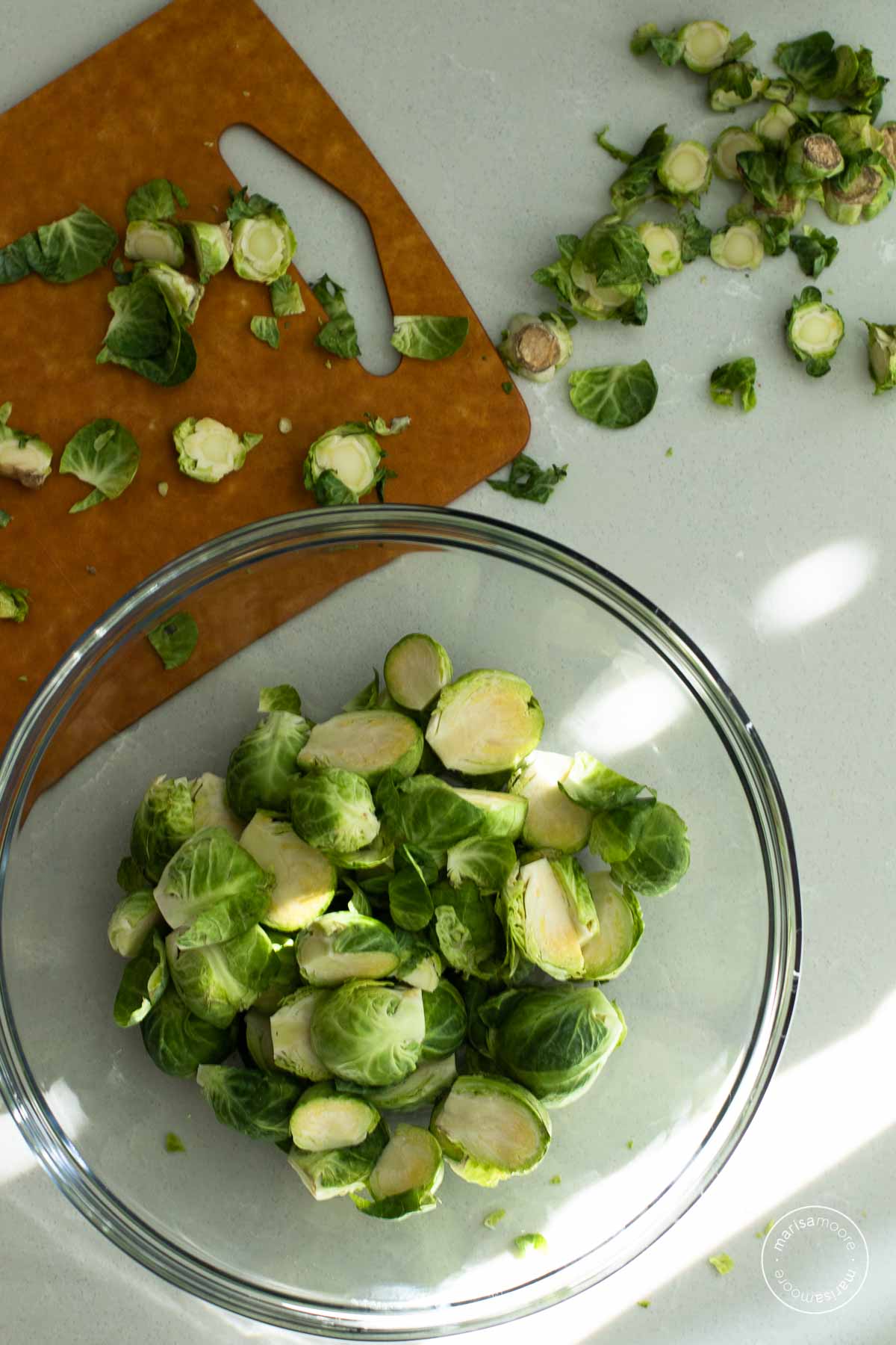 Cutting board and glass bowl with brussels sprouts being sliced
