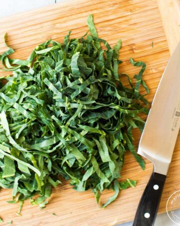 Thinly sliced collard greens on a cutting board with a knife.