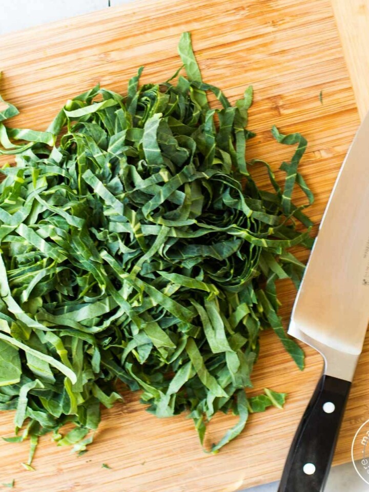 Thinly sliced collard greens on a cutting board with a knife.