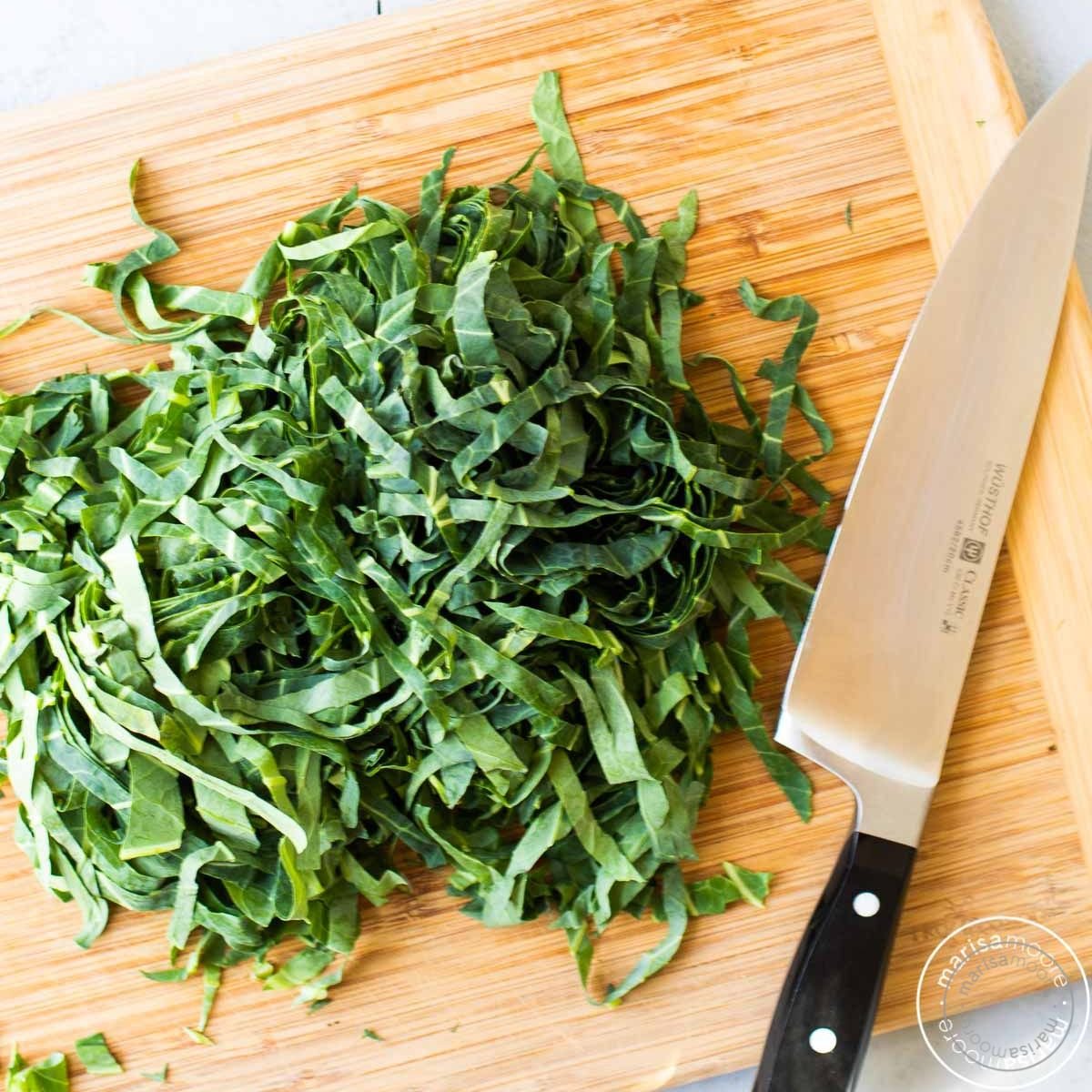 Thinly sliced collard greens on a cutting board with a knife.