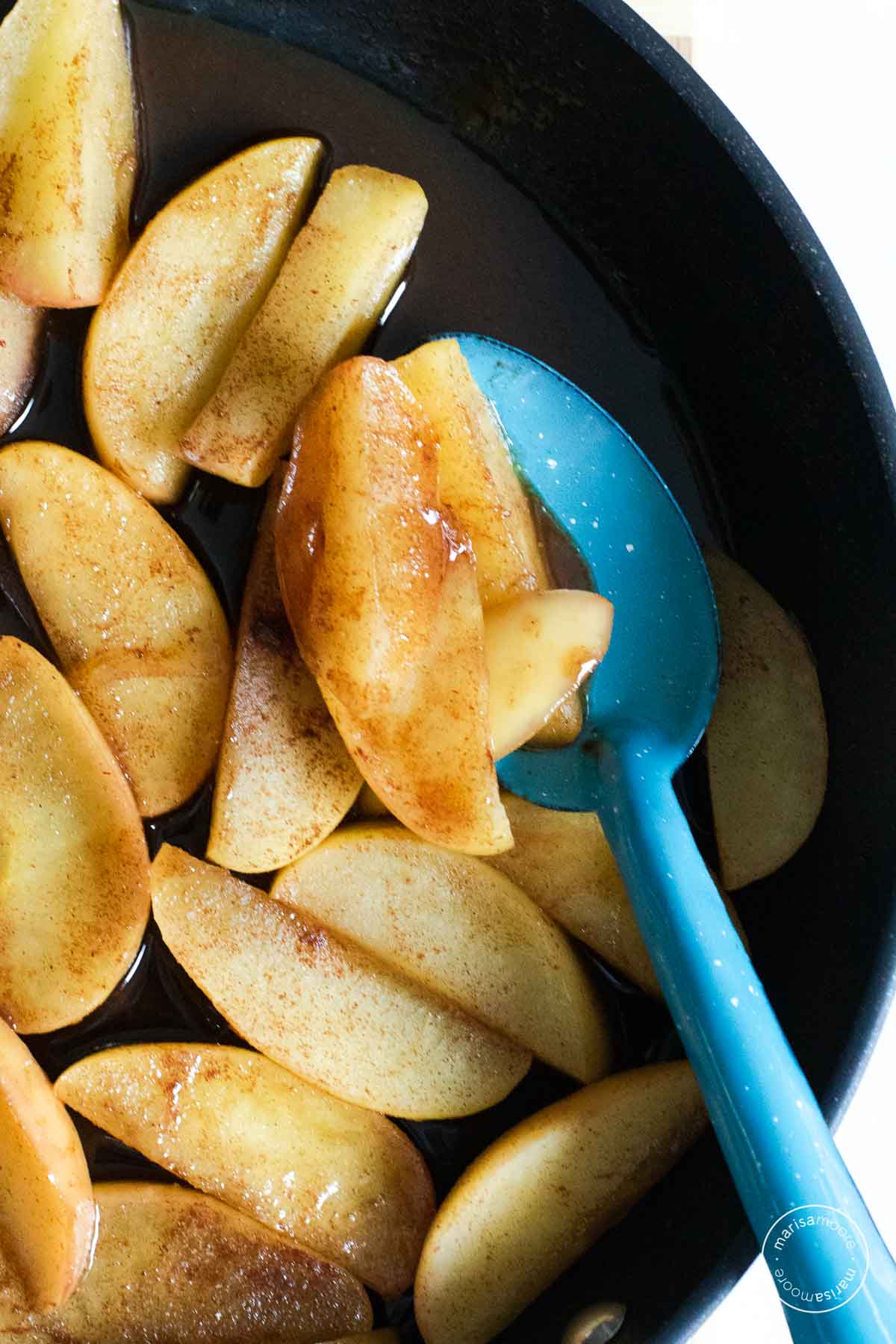 Apples in a skillet with a blue spoon