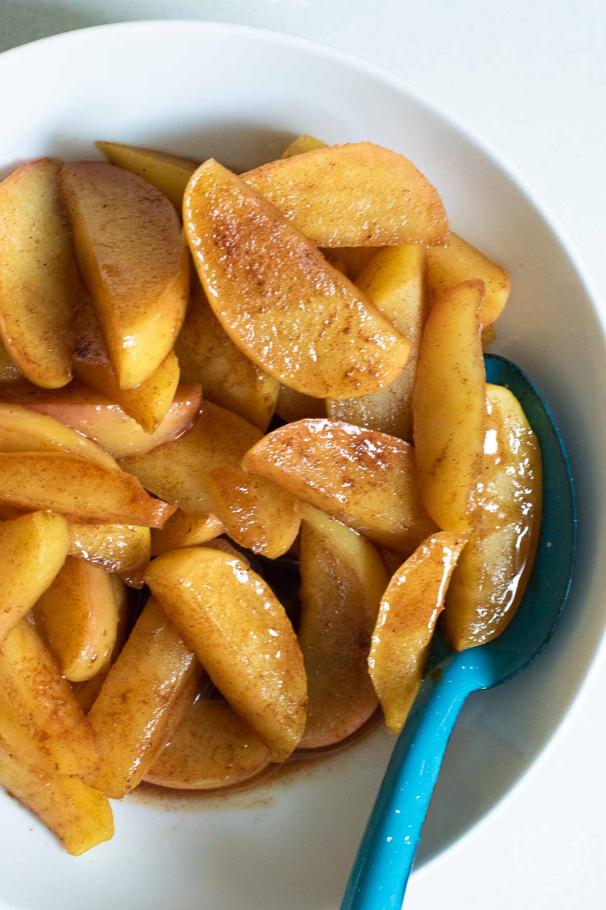 Cinnamon apples in a white bowl with a blue spoon