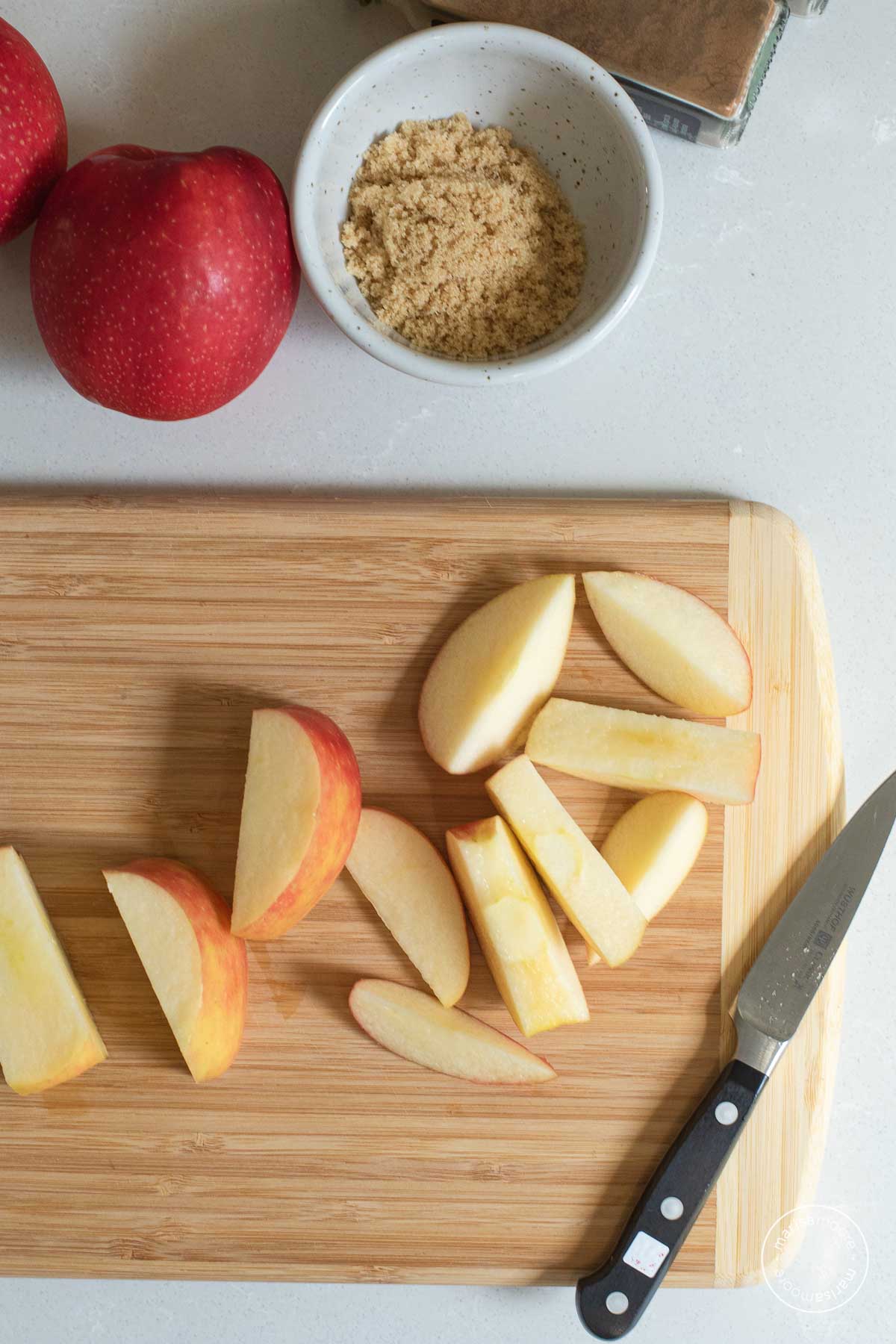 Cut apples on a cutting board plus brown sugar in a bowl.