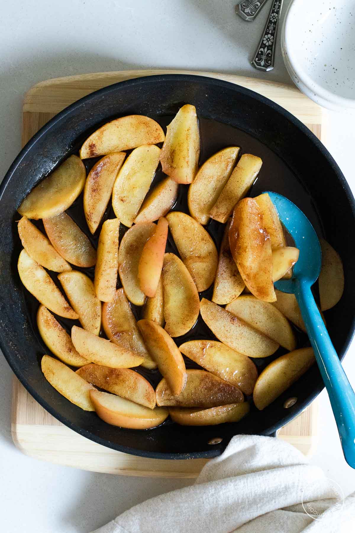 Apples in a skillet with a large blue spoon