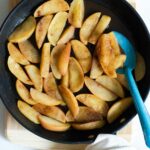 Cooked cinnamon apples in a black skillet with a blue spoon.