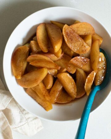 Cooked cinnamon apples in a white bowl with a blue spoon.