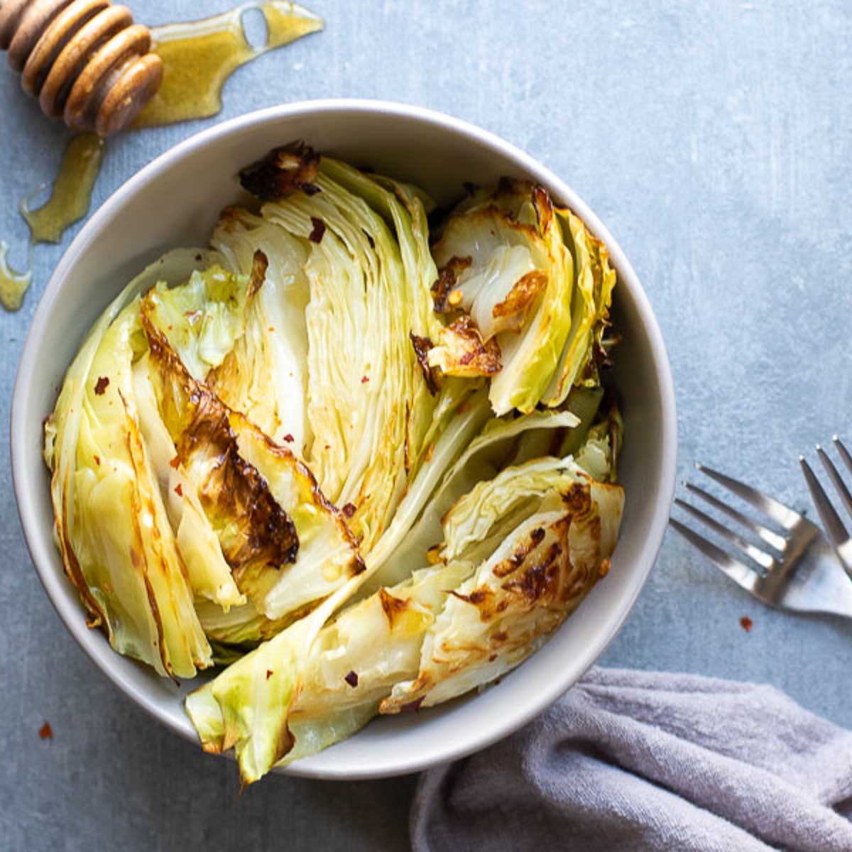 Bowl of roasted cabbage with a spool of hone on the side.