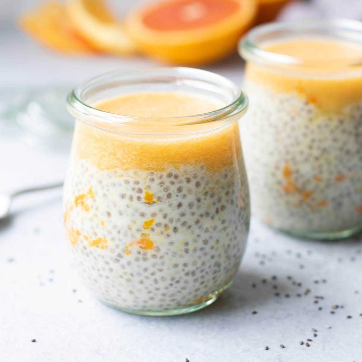 Creamsicle chia pudding in jars with oranges in background.
