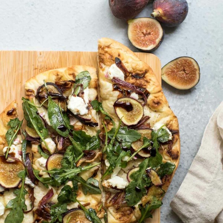 Fig and Cheese Flatbread on a wooden cutting board with a beige napkin on the side.