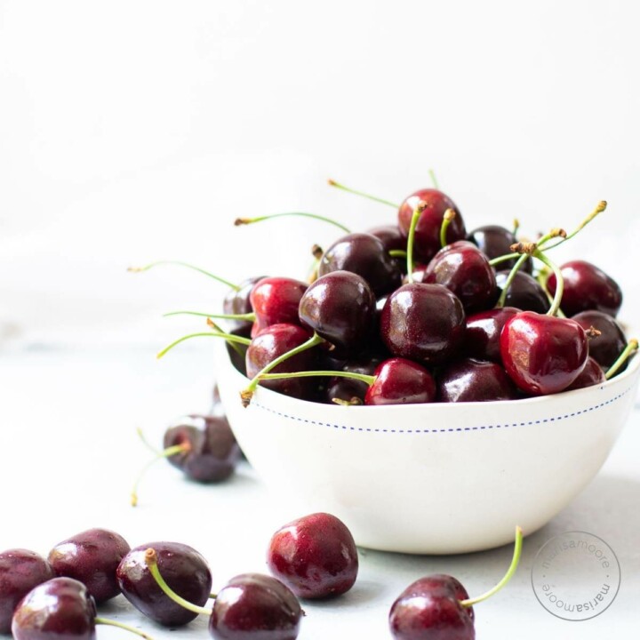 Fresh cherries overflowing and in a white bowl.