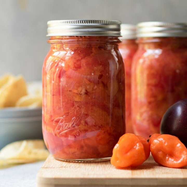 plum habanero salsa in jars with fresh peppers and plums in the foreground