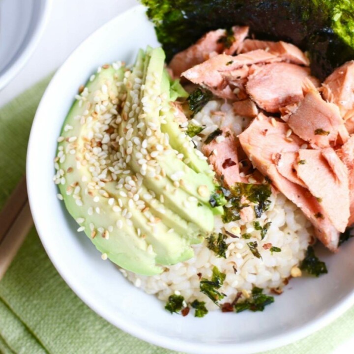 Avocado, salmon, rice and nori in a bowl with sesame sprinkled on top.