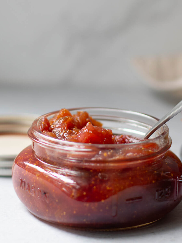Fig jam in a flat wide jar with a spoon inserted.