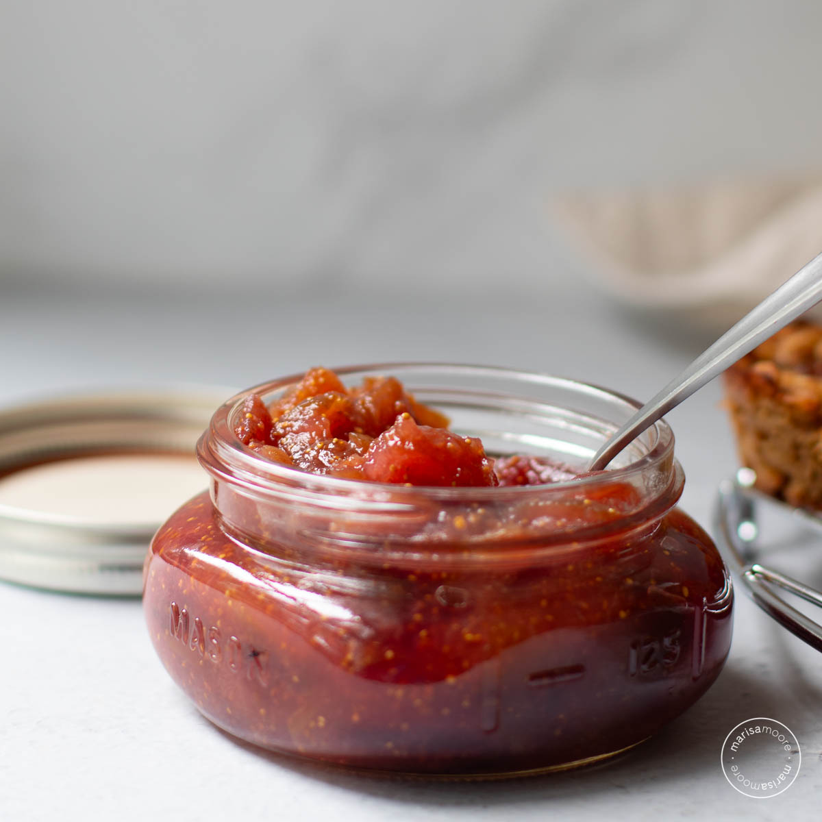 Fig jam in a flat wide jar with a spoon inserted.